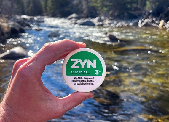 ZYN Spearmint 3mg pouch by a stream, held in hand outdoors